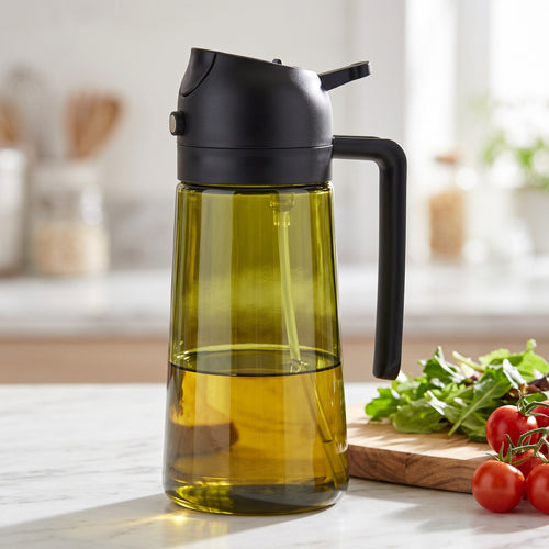 Transparent olive-green bottle with a black sprayer and handle, on a kitchen counter near salad greens