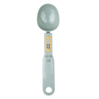 Light gray digital measuring spoon scale with LCD display and buttons shown from overhead view