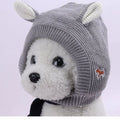 Gray knitted dog ear muffs with white ear accents on a fluffy white dog, shown from the side
