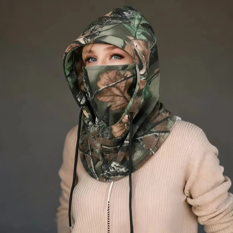 Person wearing a green and brown leaf-pattern fleece balaclava with hood and face covering, indoors