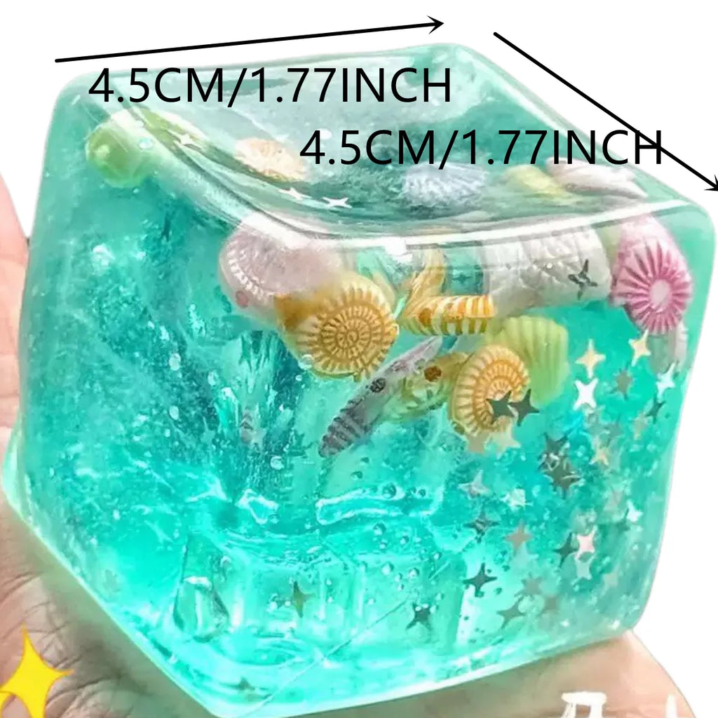 Transparent teal squishy block fidget toy with mini sea shells and stars, held in a hand, 4.5 cm wide