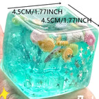 Transparent teal squishy block fidget toy with mini sea shells and stars, held in a hand, 4.5 cm wide