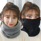Woman wearing a grey knitted neck warmer and a black neck warmer pulled up over her face, indoors