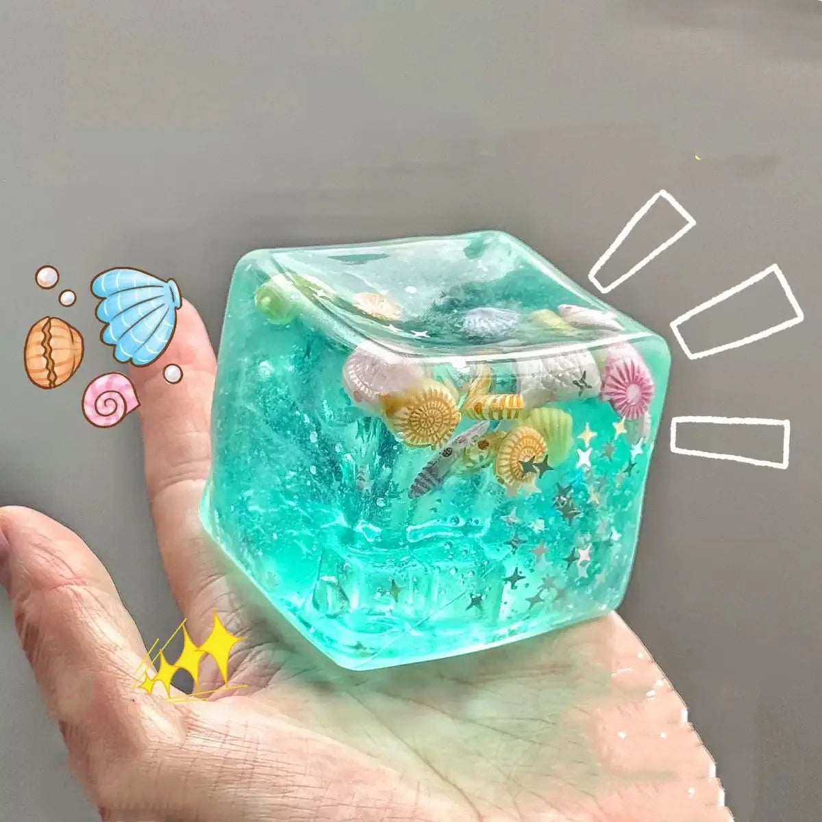 Translucent blue squishy cube fidget toy with small ocean-themed decorations, shown in a hand