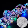 Silver ribbon string lights with snowflake and star patterns, glowing in multicolor on a dark surface, with a small inset showing the unlit ribbon