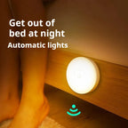 Round white motion sensor night light glowing on a wooden bed frame near bare feet on carpet
