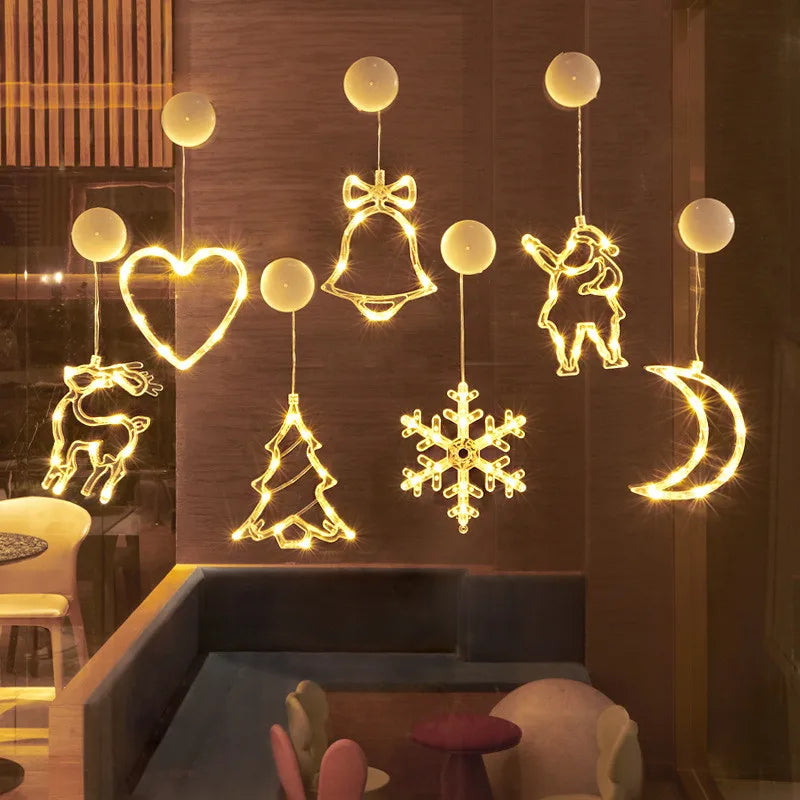 Seven yellow LED Christmas ornaments in heart, bell, reindeer, tree, snowflake, Santa, and moon shapes hanging on a window
