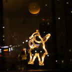 Warm white LED Christmas ornament shaped like a dancing figure, hanging on a window at night