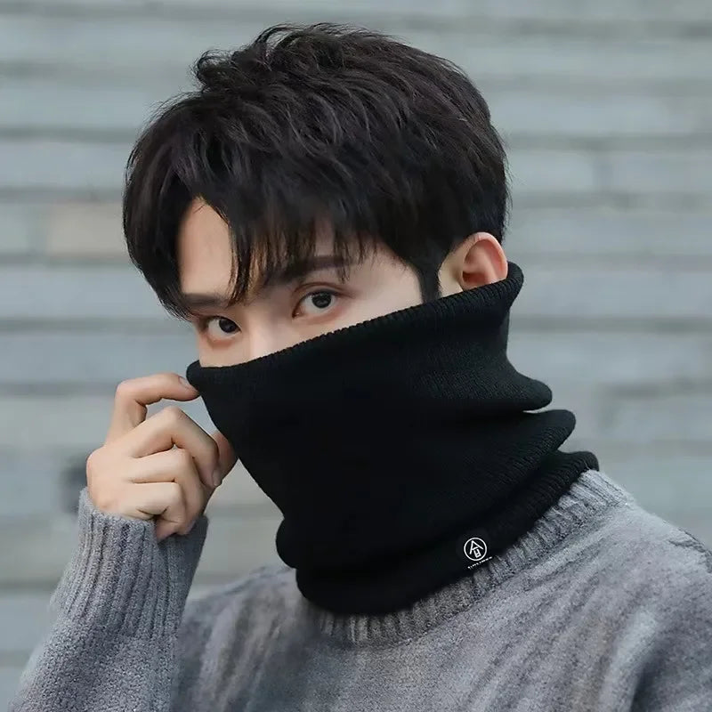 Man wearing a black knitted neck warmer covering nose and mouth, paired with a grey sweater