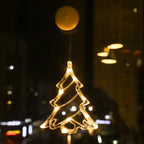 Warm white LED Christmas tree ornament hanging on a window with city lights in the background