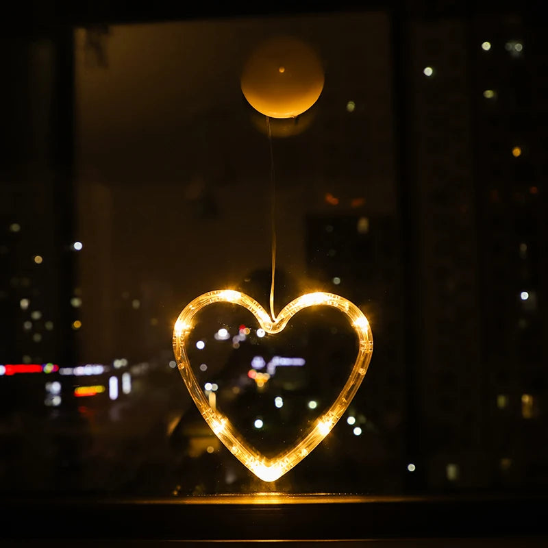Heart-shaped warm white LED ornament hanging from a window, glowing against a night city view