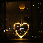 Heart-shaped warm white LED ornament hanging from a window, glowing against a night city view