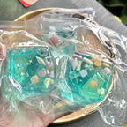 Two transparent aqua blue squishy blocks with tiny seashells and star shapes, held in a hand