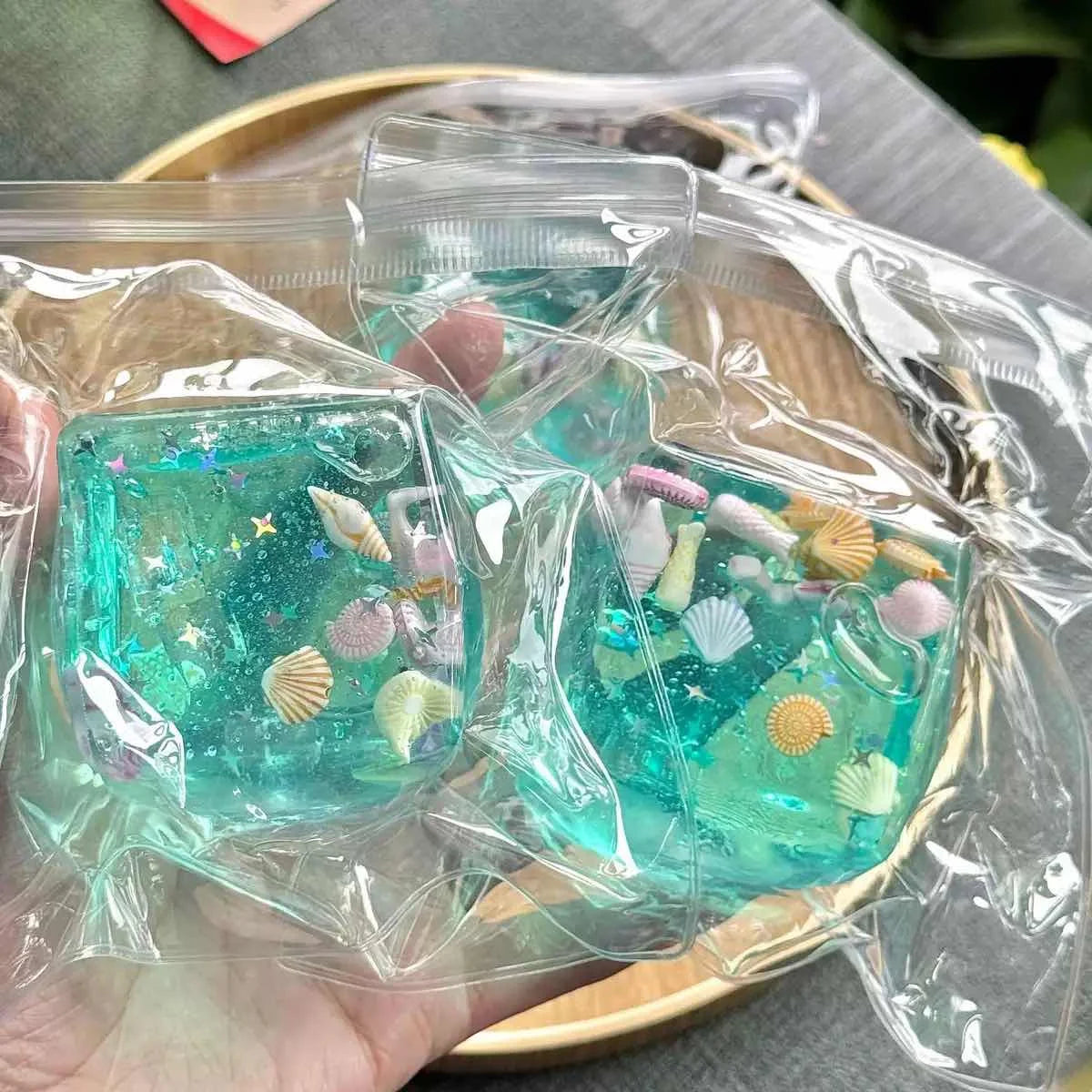 Two transparent aqua blue squishy blocks with tiny seashells and star shapes, held in a hand