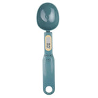 Teal digital measuring spoon scale with LCD screen and buttons, shown from above on a white background