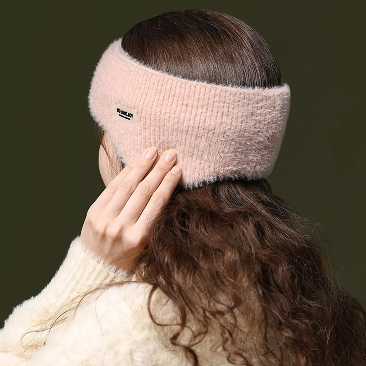 Soft light pink fuzzy ear warmer headband worn on a woman with long brown hair, rear view