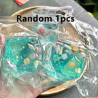 Square blue-green squishy blocks with tiny shell shapes inside, shown in a hand inside clear bags