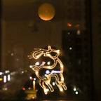 Warm white LED reindeer ornament hanging from a window at night with city lights in the background