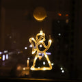 Warm white LED angel ornament hanging in a window at night with city lights in the background
