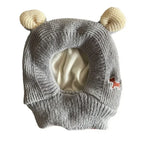 Gray knitted dog ear muffs with cream-colored ear details and a small red dog patch, laid flat