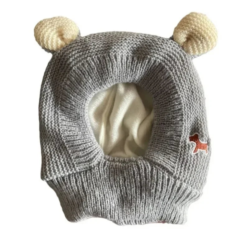 Gray knitted dog ear muffs with cream-colored ear details and a small red dog patch, laid flat