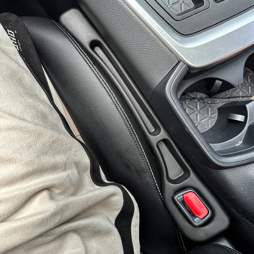 Black car seat gap filler installed between a car seat and center console, next to a seatbelt buckle