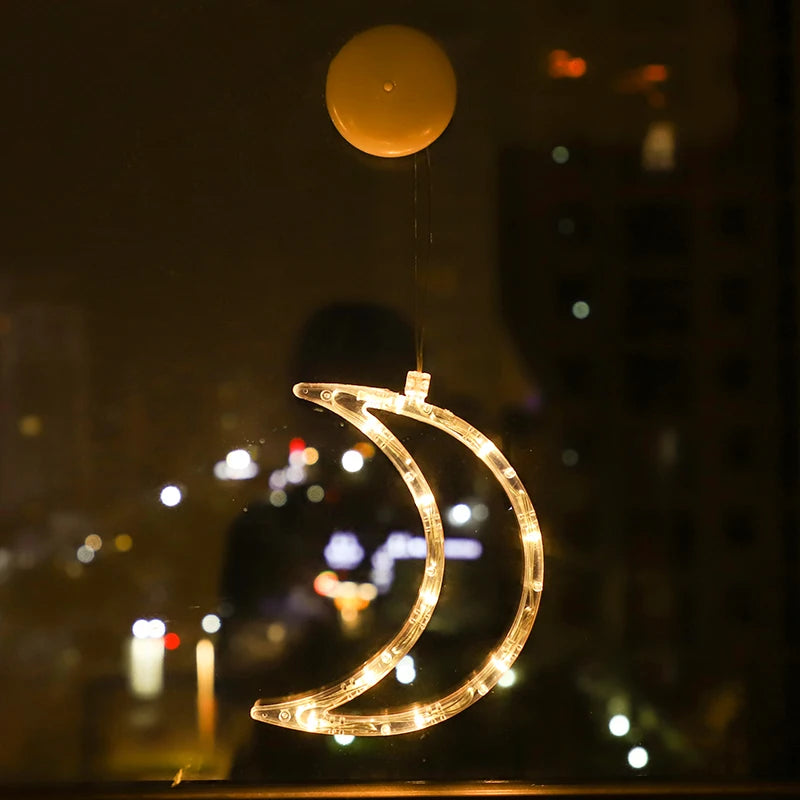 Crescent moon-shaped clear LED ornament glowing warm white, hanging on a window at night