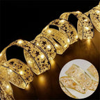 Gold ribbon string lights with star and snowflake patterns, glowing on a dark surface, close-up view