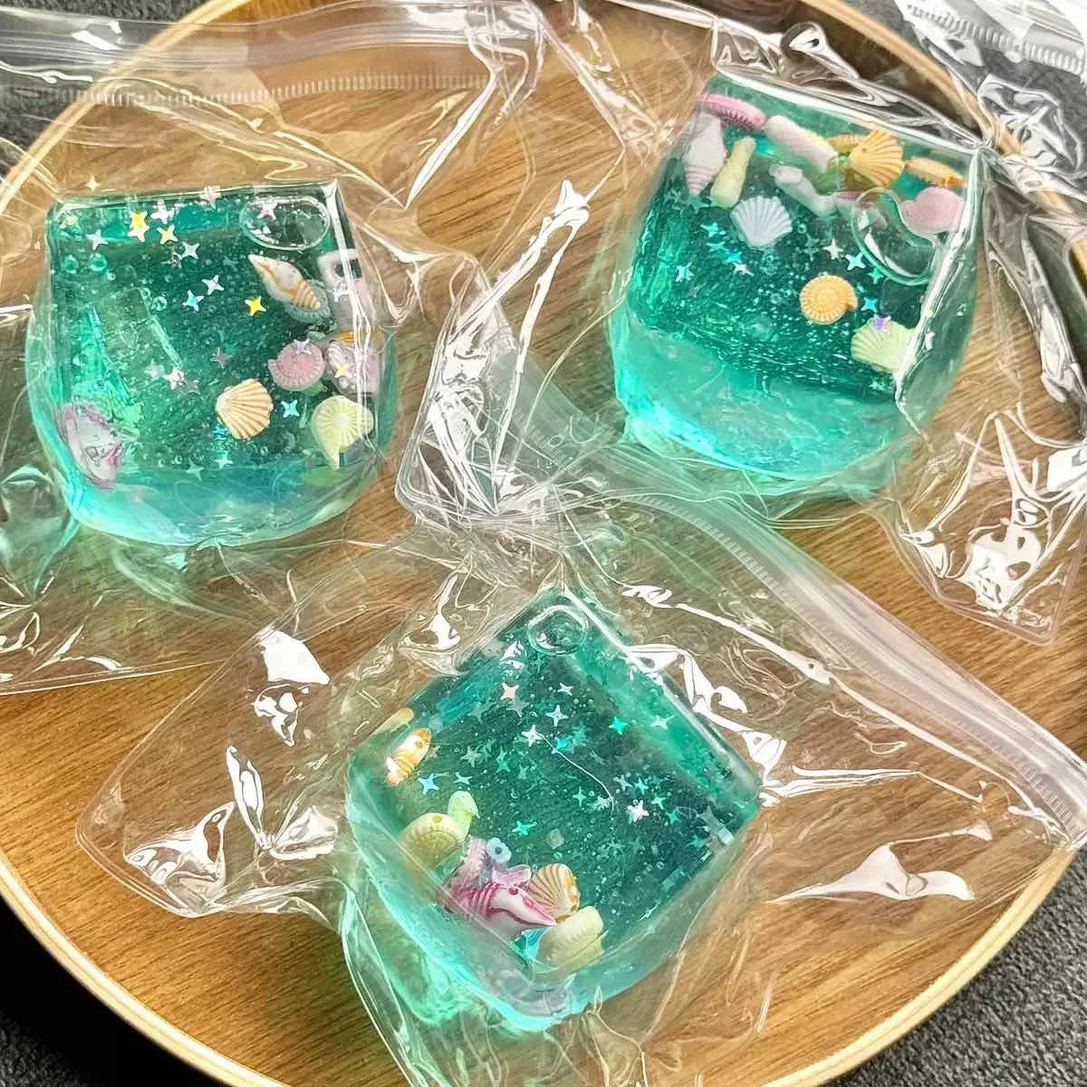 Three blue-green squishy fidget blocks with tiny seashells and stars, sealed in clear plastic bags