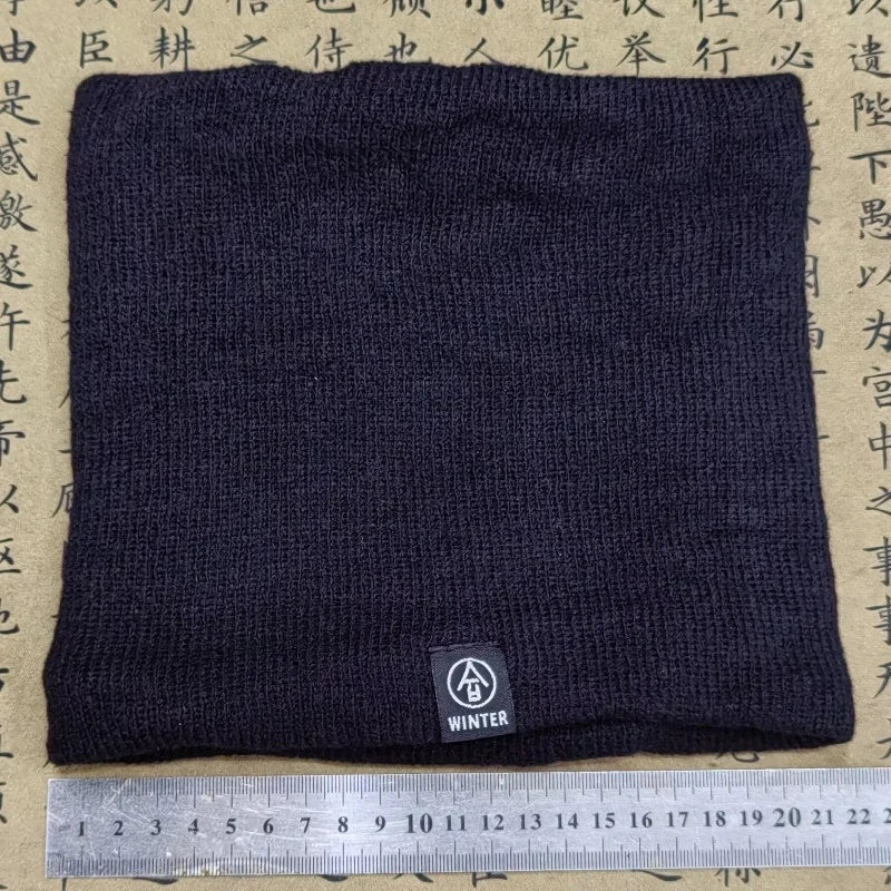 Black knitted neck warmer laid flat on a surface with a ruler for scale, tag showing "WINTER