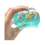 Translucent blue squishy fidget toy with shells and stars inside, held in a person's hand
