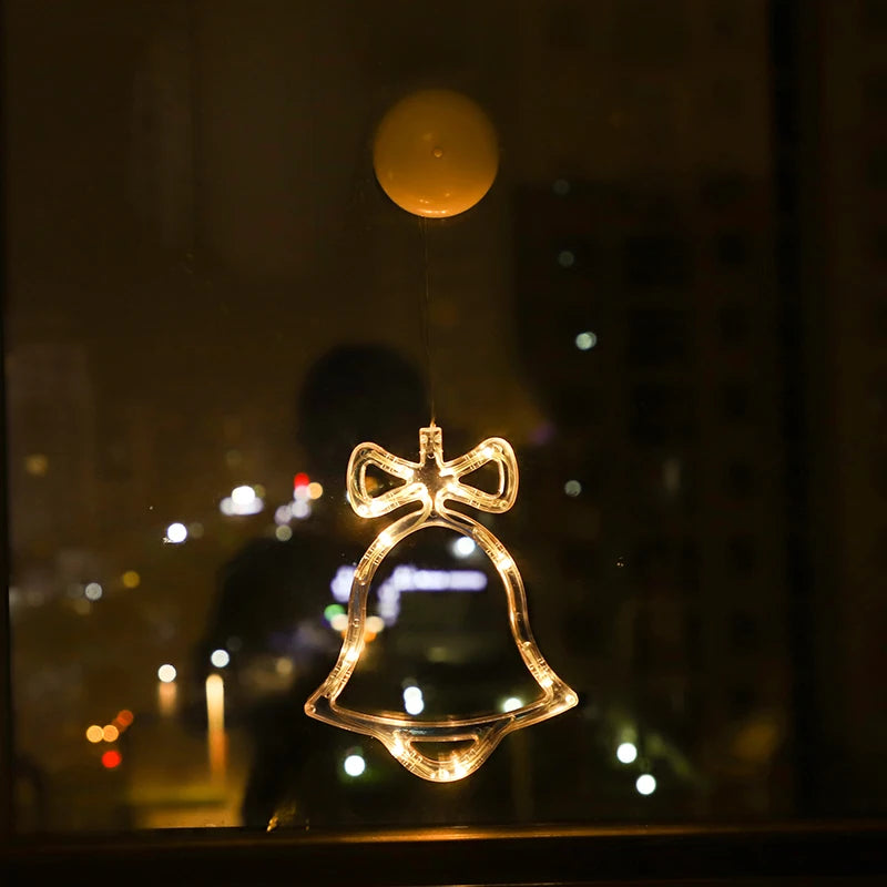Clear LED bell-shaped ornament with a bow, glowing warm white, hanging on a window at night