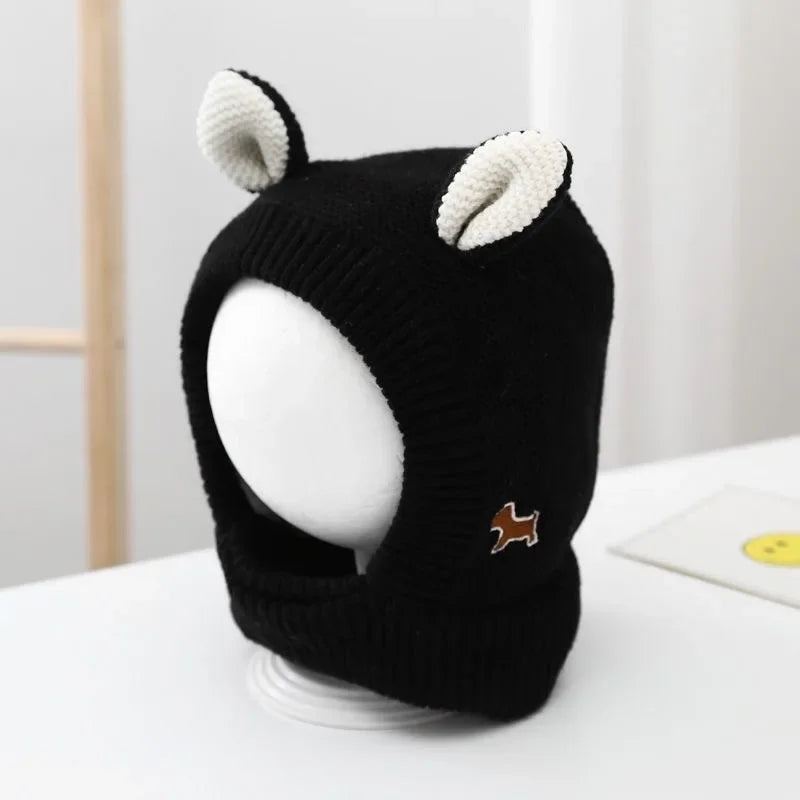 Black knitted dog ear muffs with white inner ears on display, featuring a small brown dog patch