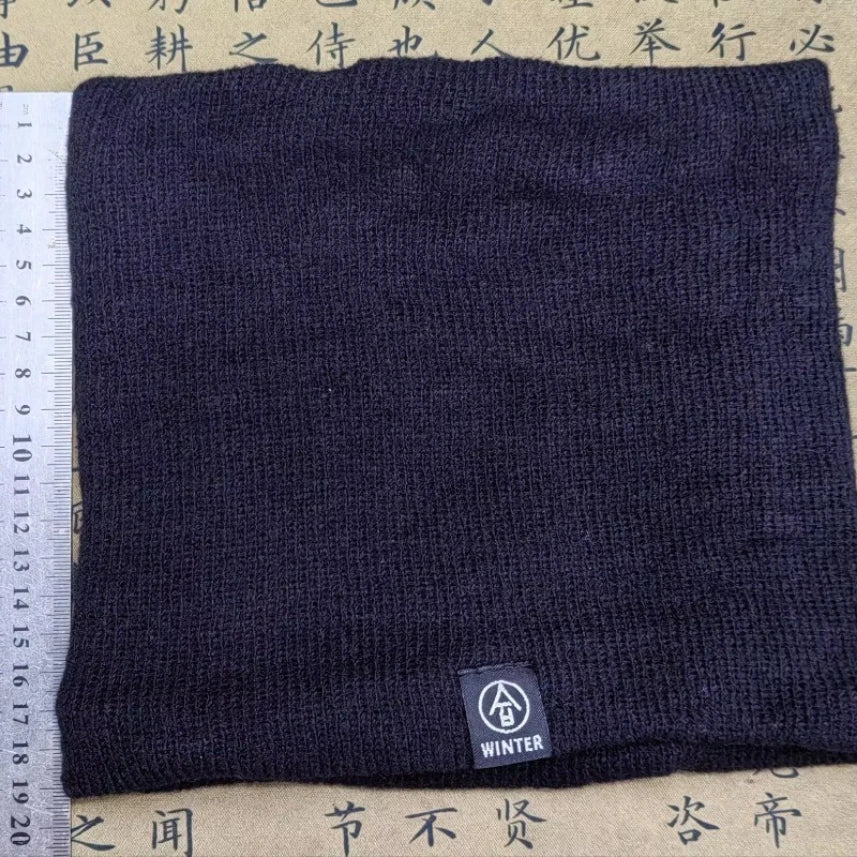 Black knitted neck warmer laid flat with a measuring ruler beside it, tag labeled "WINTER" visible