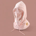 Pale pink fleece winter hood with drawstrings and a patch, displayed on a plain mauve background