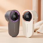 Two rechargeable lint removers, one grey with purple trim and one white with rose gold trim, standing on a beige surface